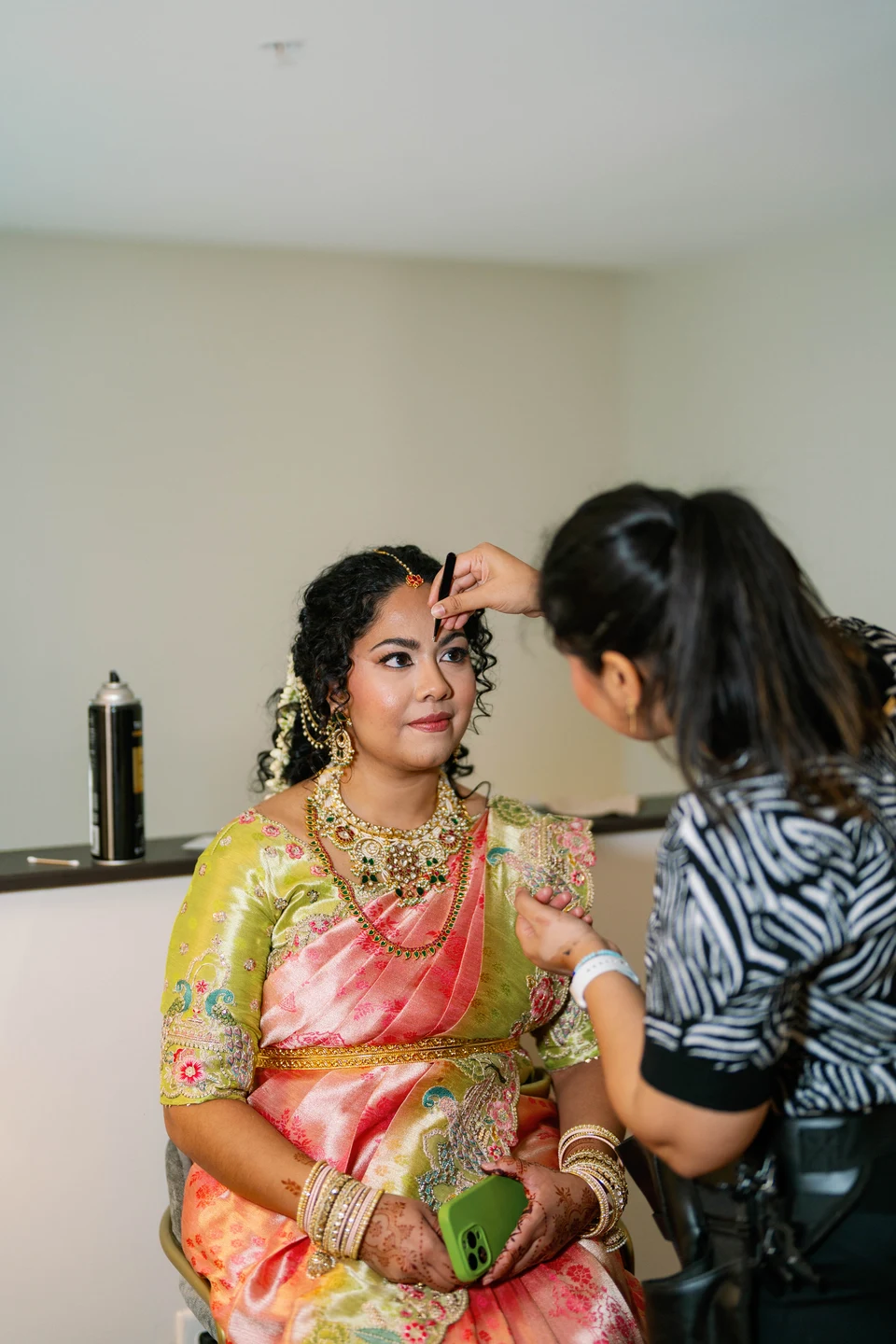 Amulya carefully applying eye makeup to a bride in a pink silk saree