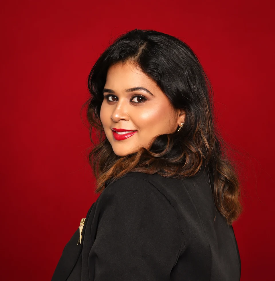 Amulya, makeup and hair artist, smiling over her shoulder against a deep red background