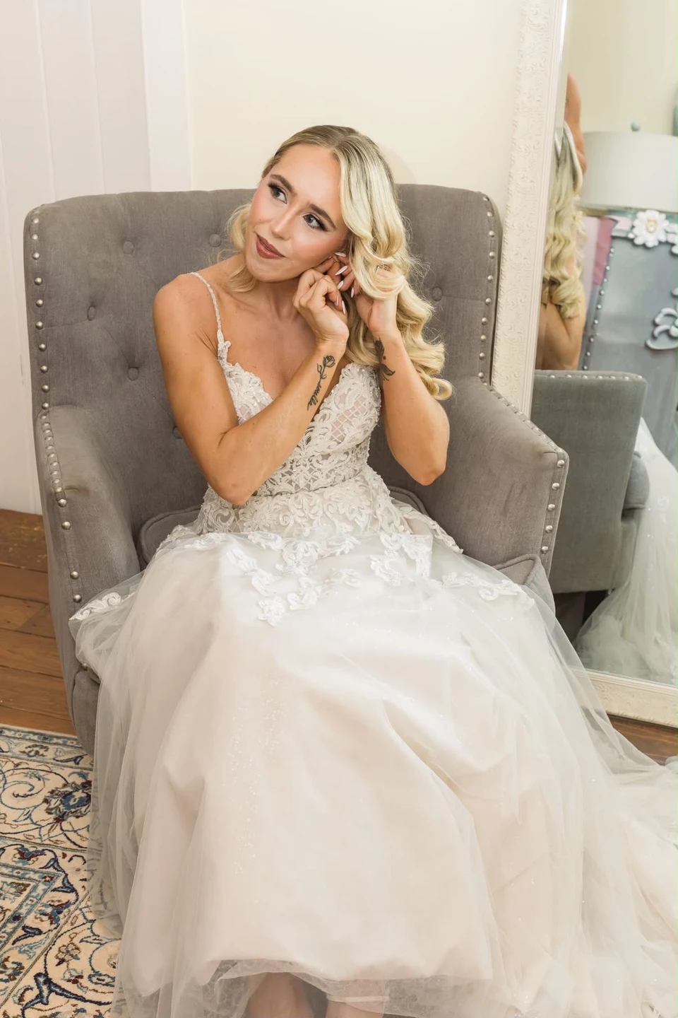 Bride in a white lace gown adjusting an earring, with softly waved hair
