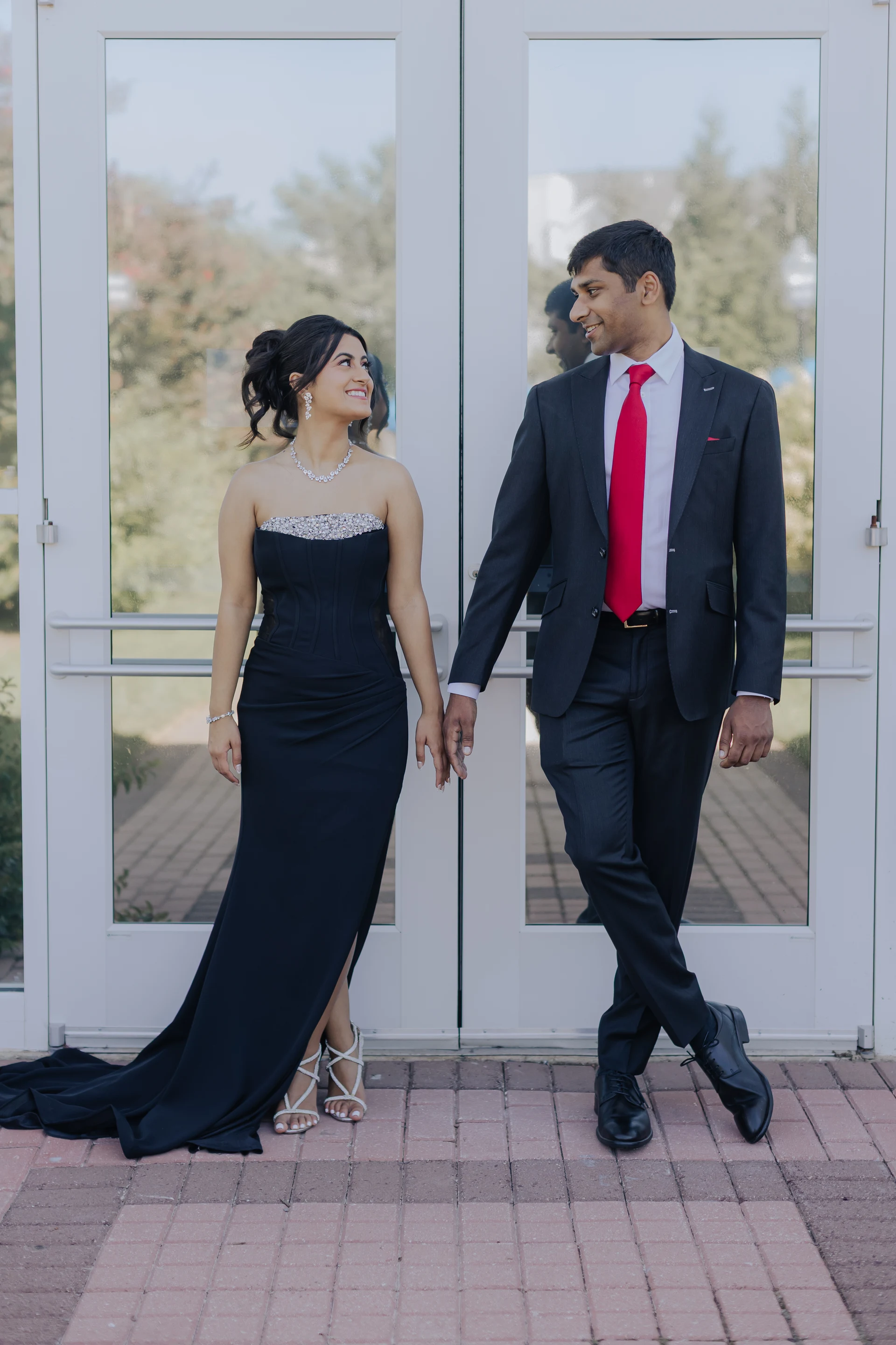 Couple holding hands, with a swept-up hairstyle and a black evening gown