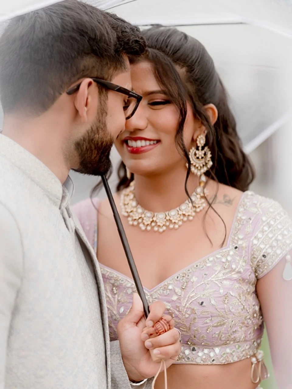 Couple beneath an umbrella, with the bride in a sparkling pastel outfit