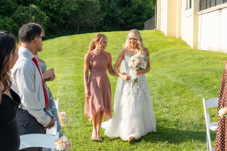 Bride in a white wedding gown holding a bouquet on a sunlit lawn during an outdoor ceremony