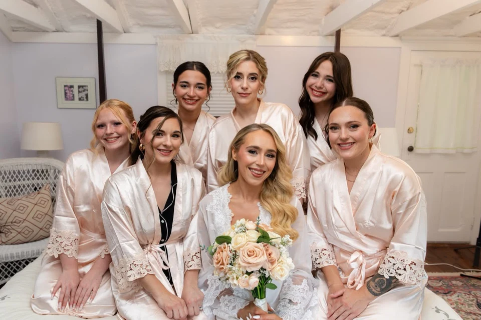 Bride holding a bouquet, surrounded by her bridal party in pale satin robes