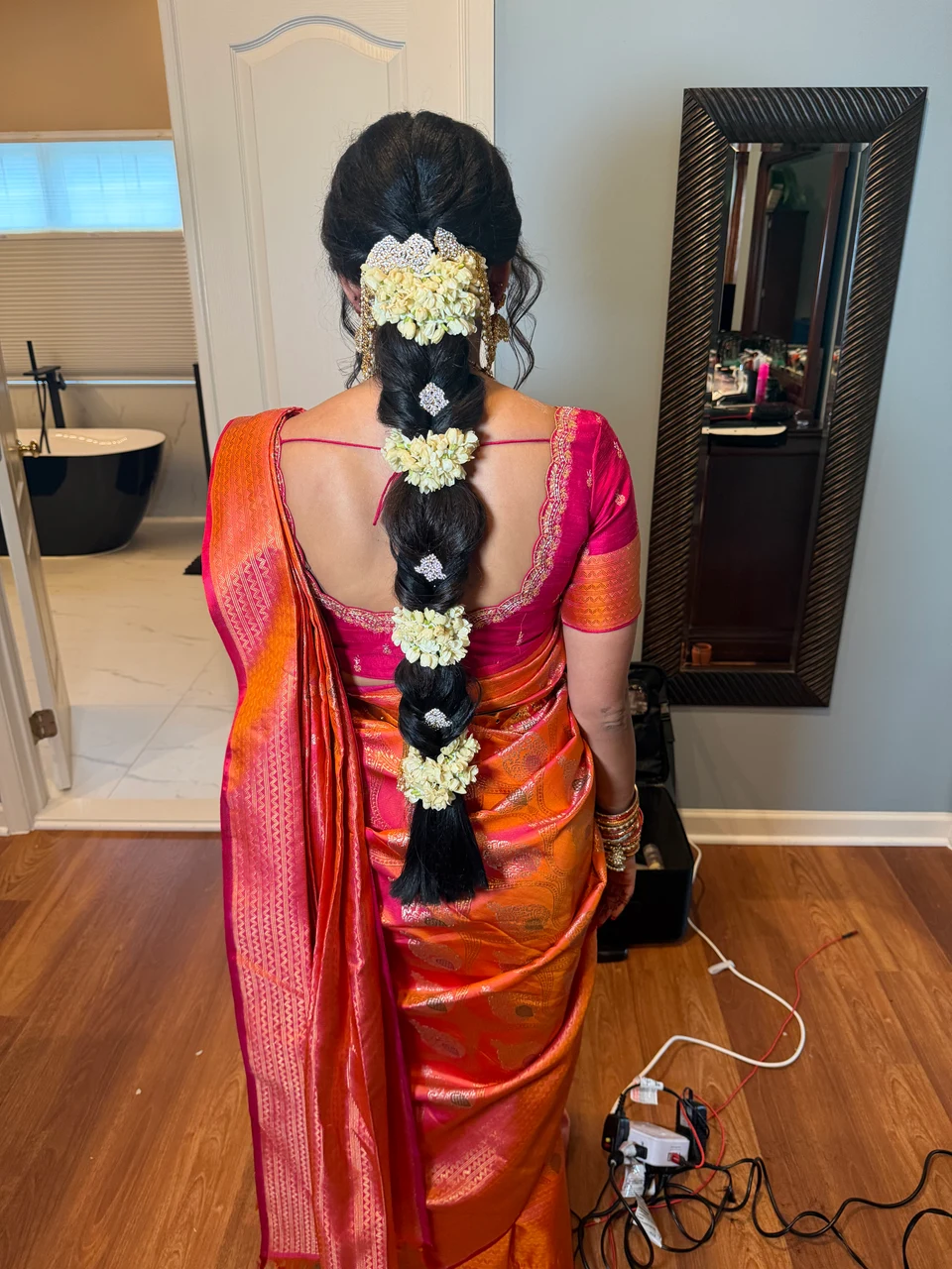 Back view of a long dark braid decorated with jasmine flowers above an orange and pink silk sari