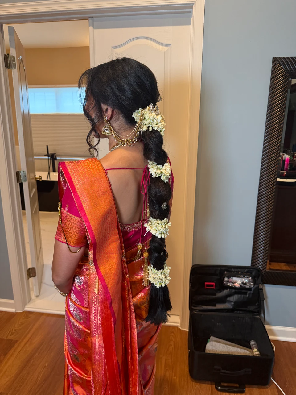 Side view of a long floral braid with jasmine accents and face-framing curls above a silk sari