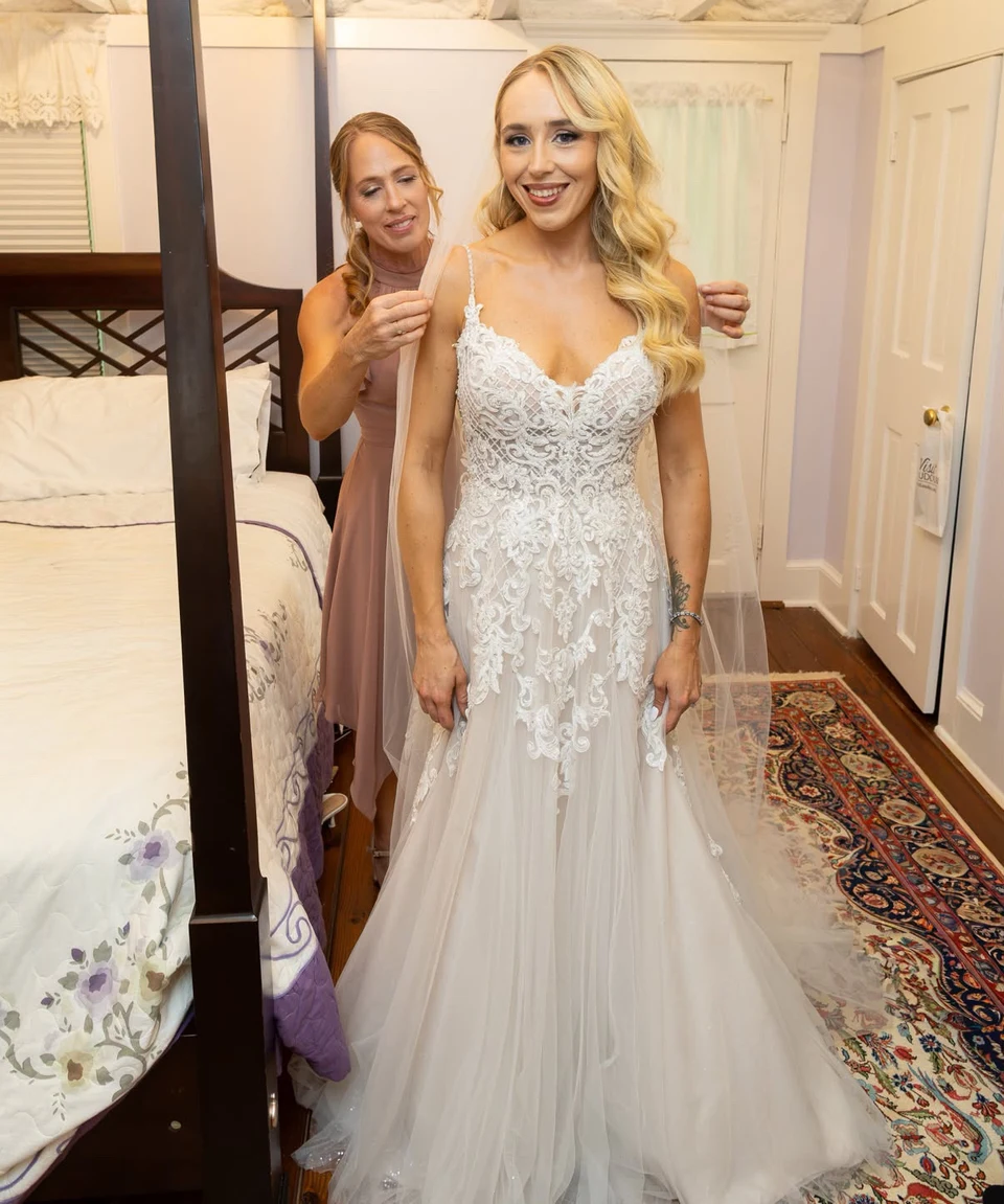 Bride in a white lace wedding gown receiving the finishing touches before her ceremony