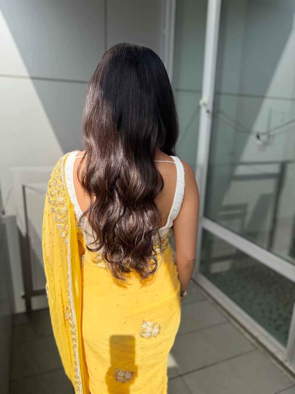 Back view of glossy dark hair falling in long loose waves above a yellow sari