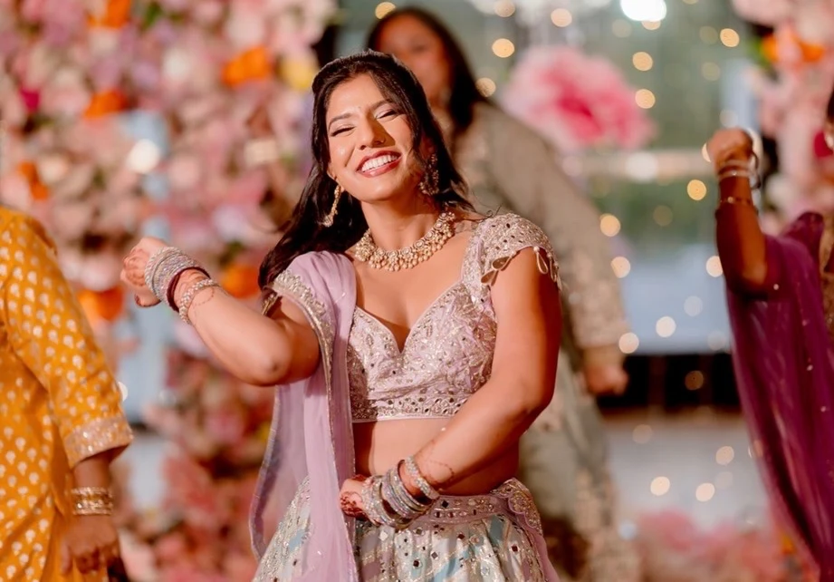 Smiling woman in a pastel embroidered lehenga dancing at a floral celebration