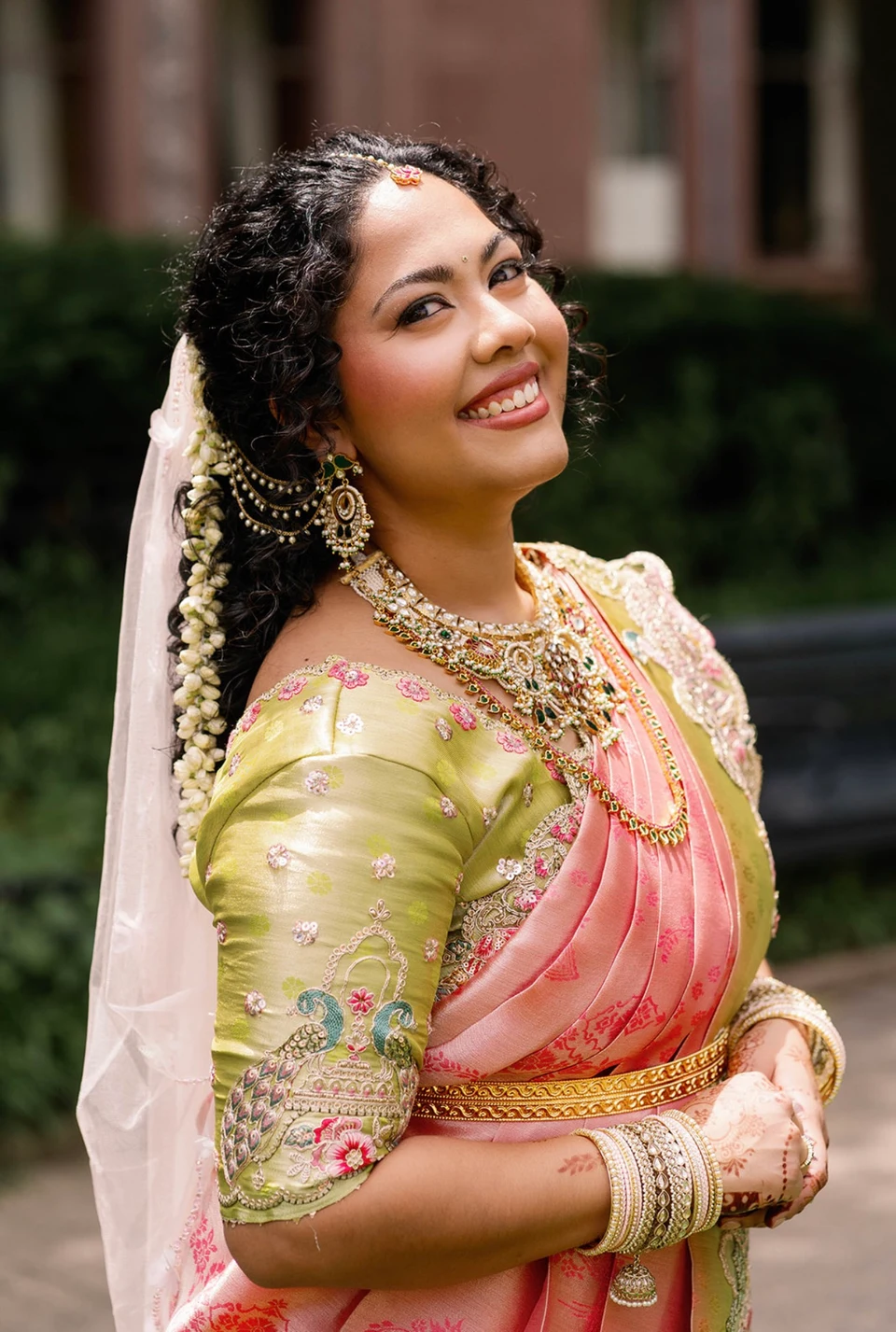 Smiling bride in a pink silk saree, green blouse and gold jewelry