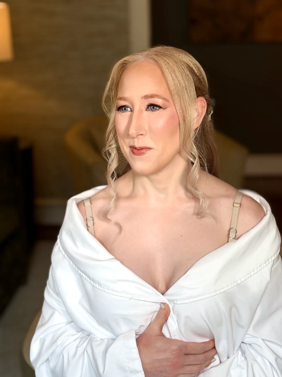 Soft bridal makeup with rosy lips and blonde face-framing curls during preparation