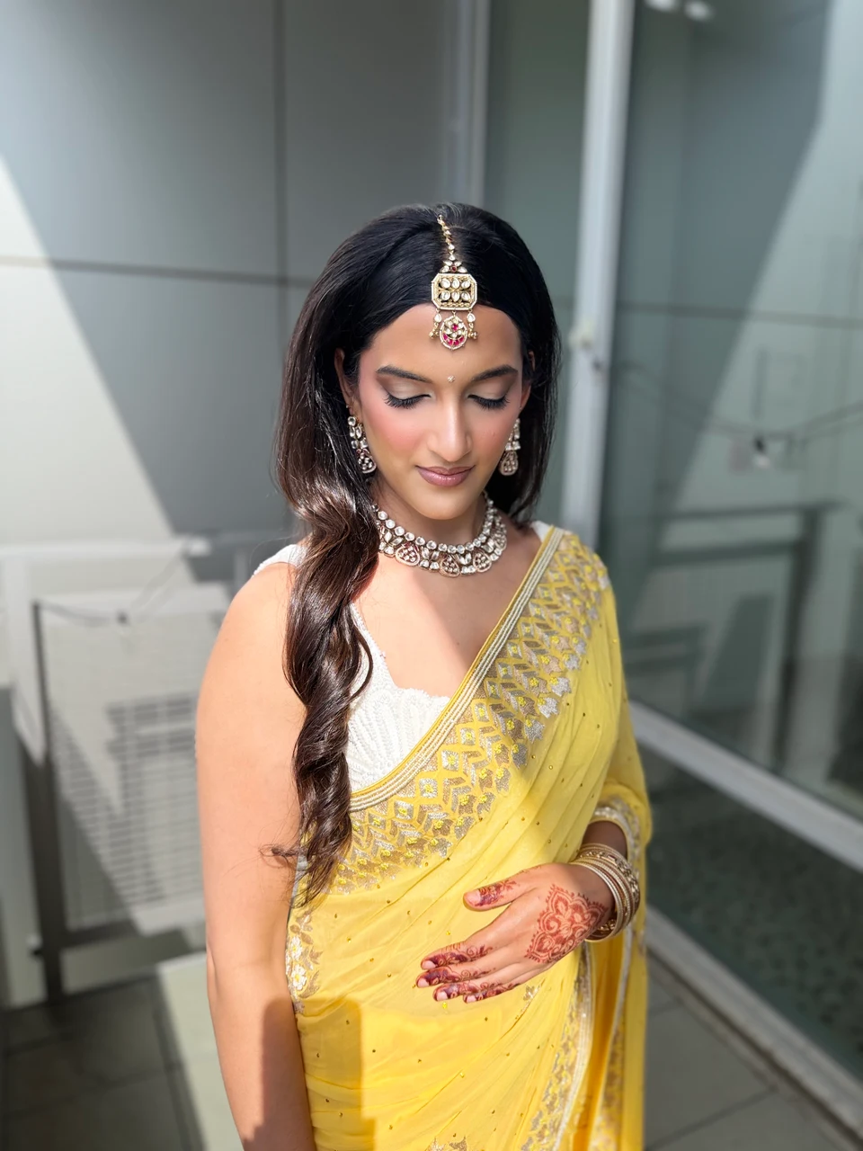 Yellow embroidered sari, jeweled hair ornament, henna and softly waved hair in a sunlit bridal portrait